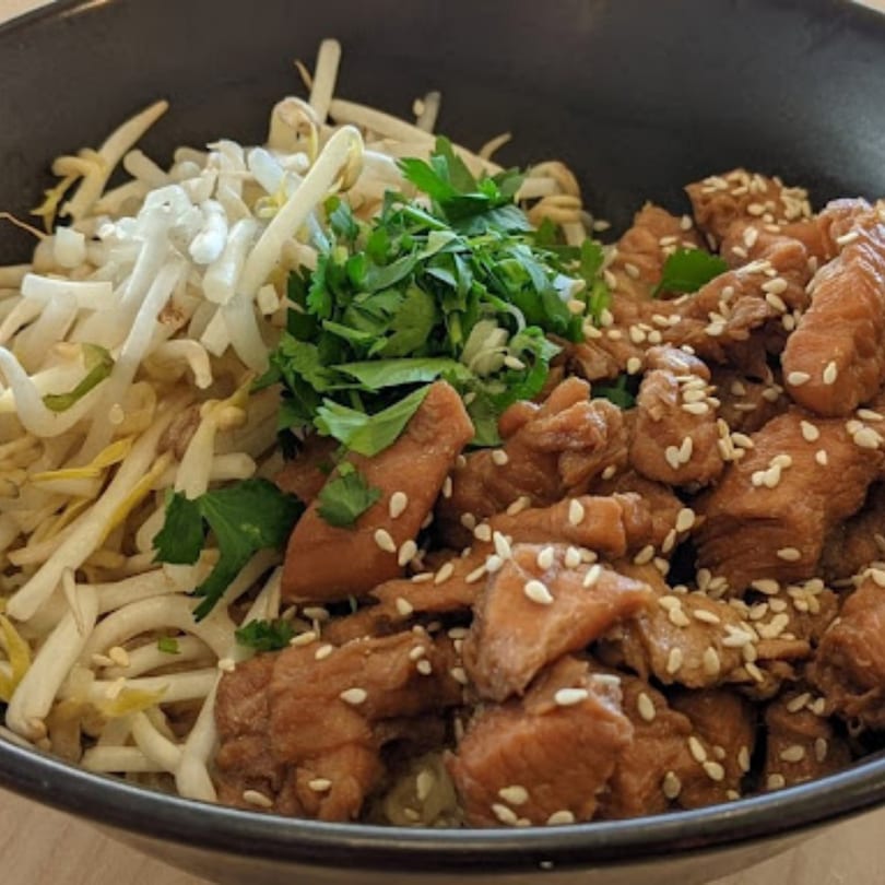 A Thai dish with chicken, bean sprouts, and fresh herbs in a dark bowl.