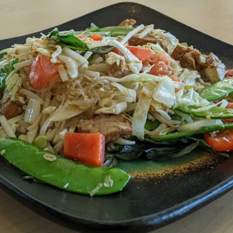 Thai glass noodle salad with chicken, tomatoes, cabbage, and snap peas on a dark plate.
